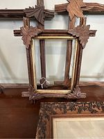 Close up of the smaller carved wooden frame with gold inner border and leaf corner carvings, showing missing parts on the carved leaves.