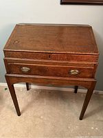 Front view of antique wooden slant standing desk showing patina and drawer pull hardware.