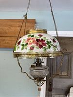 Full view of antique hanging oil lamp showing floral hand-painted glass shade with brass frame and chain.