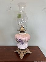 Full view of the antique hand-painted oil lamp showing pink textured glass body with floral designs, brass base and clear chimney.