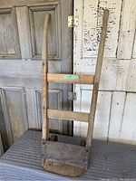 Front view of the antique wooden dolly showing wooden handles and metal base plate.