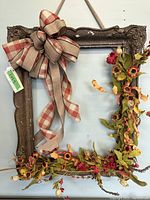 Full view of the antique rectangular dark wood frame with attached autumn floral wreath along the bottom and right side, with a large plaid bow on the top left corner.