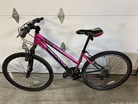 Full side view of the bike showing pink frame, black front suspension fork, wheels, pedals and handlebar.