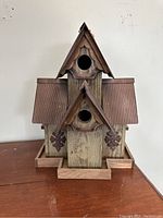 Front view showing main entrance holes, wooden body, decorative flower-shaped metal accents, and corrugated metal roofs.