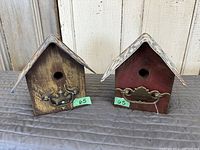 Two handmade wooden birdhouses front view with license plate roofs and metal hardware on front.