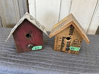 Two handcrafted birdhouses displayed side by side; one red with metal knob and the other decorated with printed paper elements.