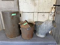 Photo showing all three items side by side: large cylindrical metal canister, rusty metal pail with hinged lid and spout, and galvanized coal shuttle with wooden handle.