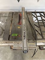 Close up of the saw table surface showing the laser line guide along the fence, worn metal table top, and power cord.