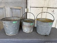 Three vintage galvanized metal pails arranged size order from left to right showing aging and patina.