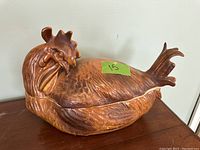 Side angle of the brown ceramic covered dish shaped like a chicken, showing the detailed sculpted feathers, comb and tail.