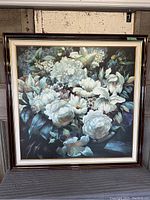 Full view of the framed floral print painting showing white flowers among dark green leaves with a dark wood frame and gold trim.