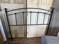Full view of black metal queen size headboard with vertical bars and rounded finials on posts.