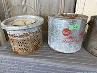 Front view of two vintage metal minnow buckets showing brand mark, rust, and wear