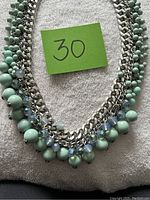 Close-up image of a statement necklace with chunky silver-tone chain and alternating mint green and blue beads.