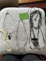 Five assorted necklaces laid out on a towel showing various styles including bead, cord, and metal chain with pendants.
