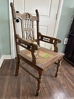 Front angled view of antique oak armchair showing carved wooden backrest, armrests, and cane seat.