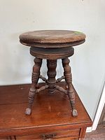 Full view of antique oak piano stool showing round wooden seat, turned legs, and glass claw feet.