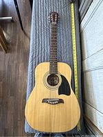Full length view of Oscar Schmidt by Washburn 3/4 acoustic guitar showing natural wood body, black pickguard, and six strings.