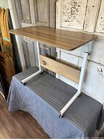 Side angle showing wooden top, white metal frame, caster wheels and wooden slat on frame.