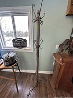 Full view of the rustic coat rack standing next to a window and furniture showing overall height, wood post and iron hooks at the top.