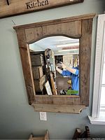 Front view of rustic wooden framed mirror with curved top and small attached shelf at bottom.