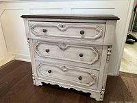 Front view of small white distressed dresser with three drawers and top wood surface.
