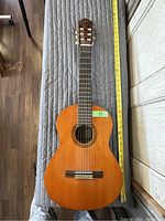 Top view of the guitar lying flat with a measuring tape showing length around 28 inches, classical style with nylon strings.