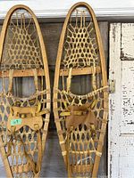Pair of traditional wooden snowshoes hanging side by side, showing overall shape and leather bindings.