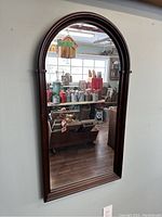 Full view of the vintage solid wood arched mirror hanging on wall showing the reflective glass and dark wood frame with curved top.
