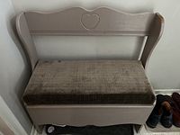 Wooden storage bench painted muted brown with dark cushioned seat and carved heart on backrest.