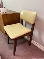Side angled view of the beige vinyl seat and back with wood frame.