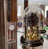 Front view of the enamelled anniversary clock under glass dome next to the pewter Charles Rennie Mackintosh designed clock.