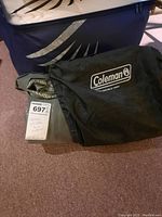 Rolled up green Coleman inflatable mattress with black storage bag on carpet.