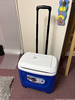 Blue and white Igloo rolling cooler with black extending handle pulled up and visible wheels underneath.