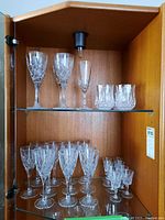 Two shelves inside a wooden cabinet filled with various sizes of cut crystal glasses including tall wine glasses, medium glasses, and short glasses.
