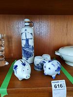 Full view of the Delft Blue collection: tall pitcher, two piggy banks, and salt and pepper shakers on wooden shelf.