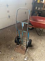 Front view of blue metal hand truck showing rust on base plate and tires