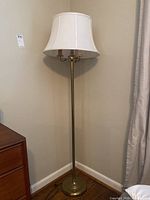Full view of the brass floor lamp with cream fabric shade showing lamp height and shape