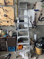Full front view of the 8-feet aluminum ladder standing upright in a garage environment surrounded by tools and cleaning supplies.
