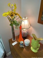 Photo of lamp, colorful glass and ceramic vases, candy dish, and faux flowers on wood surface