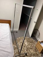 Metal clothes rack standing in a bedroom next to a bed and a decorative rug.