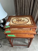 Three stacked teak nesting tables with ceramic tile tops, top view showing deer motif and size labels