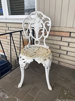 White painted metal patio chair showing front and side angles on porch floor with visible wear and weathering.