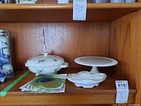 Photo showing the Rosenthal soup tureen, I. Godinger cake stand, Nippon bowl, and napkins on a wooden shelf