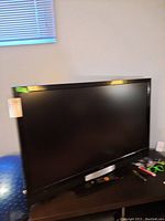 Vizio flat-screen TV positioned on a dark-colored table, showing the front black glossy frame and screen, with some items nearby.
