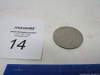 Top-down overview of the Eisenhower dollar coin near a ruler and lot card for scale reference.