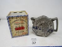 Front view of silver-tone octagonal tea pot with embossed Paul McCartney profile and original Cardew Design box.