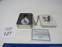Eagle pocket watch in a foam-lined tin box alongside the tin lid and Certificate of Authenticity.