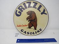 Full front view of metal round Grizzly Gasoline sign showing text and bear illustration with ruler for size reference.