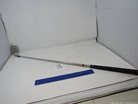 Full length photo of the Charisma golf sand wedge showing the shaft, grip, and club head on a white background with a ruler for scale